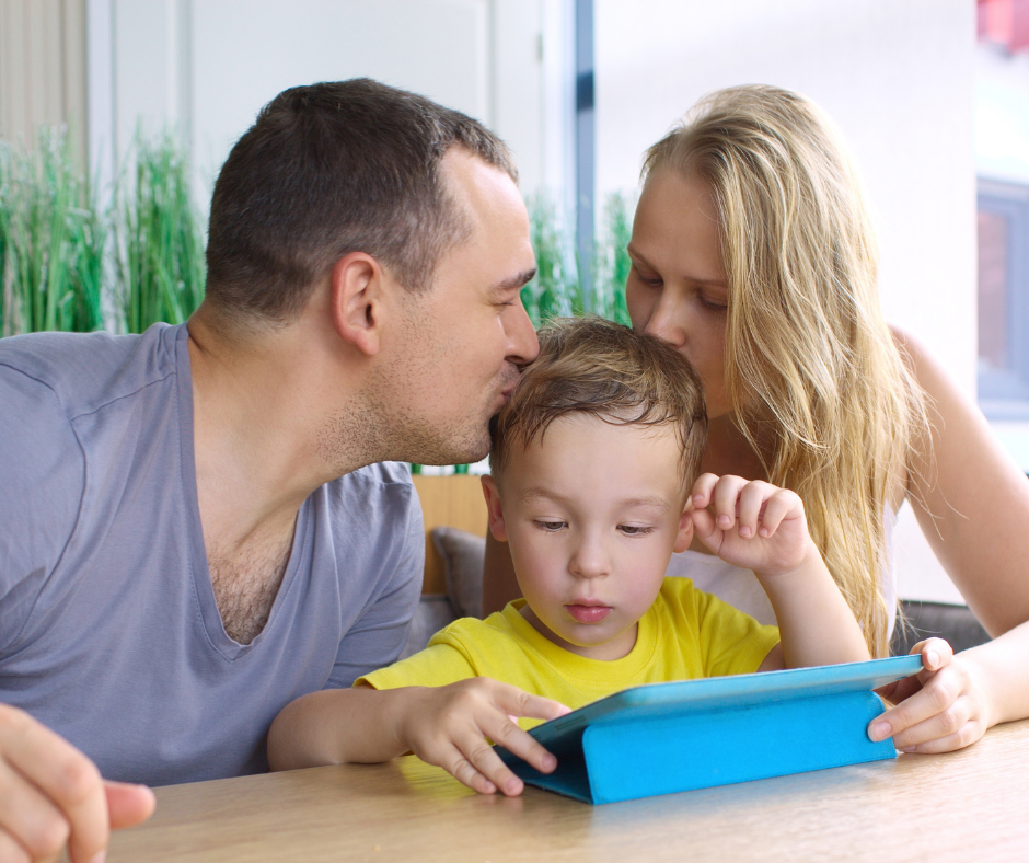 Parents kissing child using AAC on the head.