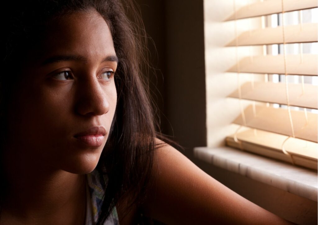 girl looking put of window looking sad